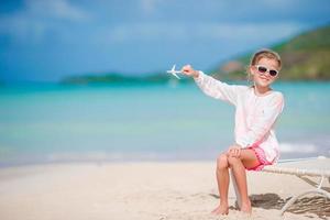 Happy little girl with toy airplane in hands on white sandy beach. Kid play with toy on the beach photo