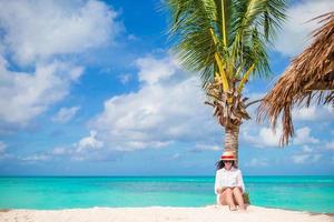 mujer joven leyendo en una playa blanca tropical cerca de una palmera foto