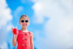 Cute little girl drinking cocktail on tropical beach photo