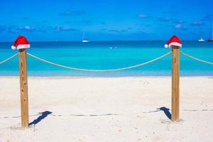 Two red Santa hats on fence at tropical white beach photo