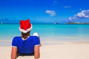 Back view of young man in santa hat on tropical beach photo