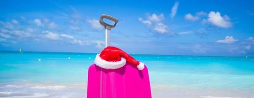 Closeup of pink suitcase and Santa Claus hat on beach photo