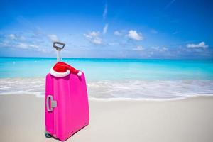 Closeup of pink suitcase and Santa Claus hat on beach photo