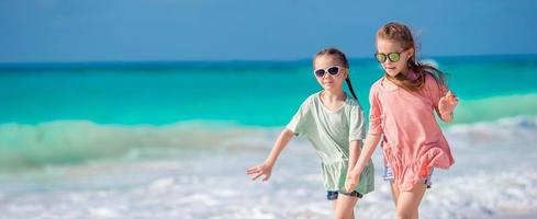 niños pequeños y felices divirtiéndose mucho en la playa tropical jugando juntos. adorables chicas bailando en la isla caribeña foto