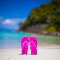 Pink vibrant beach flip flops on white sand on sea background photo