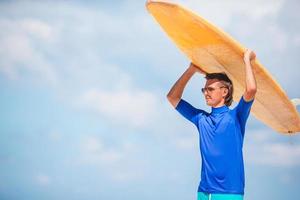 joven surfista en playa blanca con tabla de surf amarilla foto