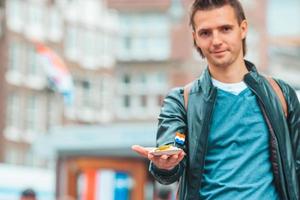 feliz turista caucásico con arenque fresco con cebolla y bandera holandesa en amsterdam. comida tradicional holandesa al aire libre foto