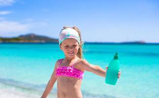 Little adorable girl in swimsuit with suntan lotion bottle photo