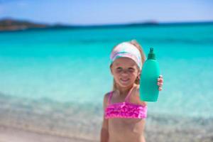 Little adorable girl in swimsuit with suntan lotion bottle photo