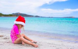 niña adorable con sombrero rojo de santa en la playa tropical foto