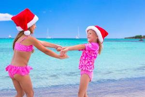 Little adorable girls in Santa hats during beach vacation photo