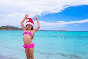 niña adorable con sombrero rojo de santa en la playa tropical foto