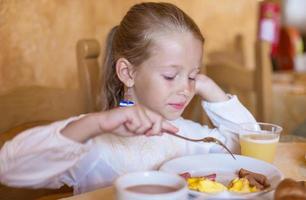 Adorable little girl having breakfast at indoor cafe photo