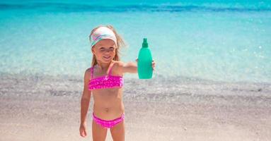 Little adorable girl in swimsuit with suntan lotion bottle photo