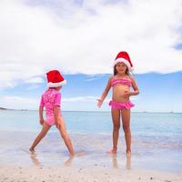 Little adorable girls in Santa hats during beach vacation photo