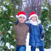 feliz padre y niño en sombreros de santa con árbol de navidad al aire libre foto