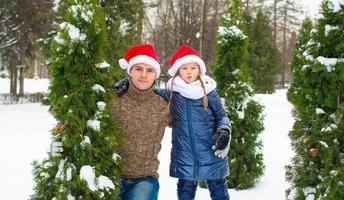 padre feliz y niña en sombreros de santa con árbol de navidad al aire libre foto