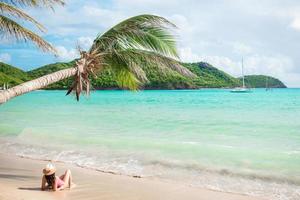 Young slim woman in bikini and straw hat lying on tropical beach. Beautiful girl under the palm tree in shallow water photo