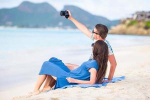 Happy couple taking a selfie photo on white beach. Two adults enjoying their vacation on tropical exotic beach