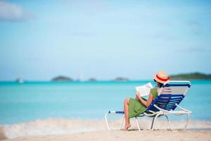 Young woman reading book on sunbeds during tropical white beach photo