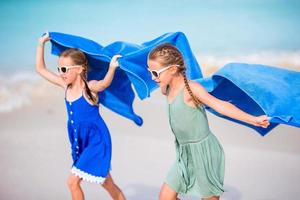 niñas lindas divirtiéndose corriendo con una toalla y disfrutando de las vacaciones en una playa tropical con arena blanca y agua turquesa del océano foto