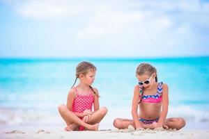 Adorable little girls playing with sand on the beach. Kids sitting in shallow water and making a sandcastle photo