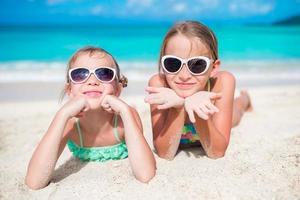 Adorable little sisters at beach during summer vacation lying on warm sand. Portrait of kids on white beach photo