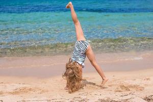 Adorable little girl making wheel on tropical white sandy beach photo