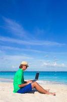 Young man with laptop on white tropical beach photo