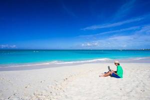 Young man with laptop on white tropical beach photo