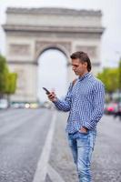 joven caucásico sosteniendo un teléfono en los campos elíseos en parís foto