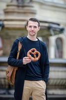 hermoso joven sosteniendo pretzel y relajándose en el parque foto