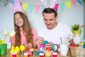 Father and his little daughter painting eggs. Happy family preparing for Easter. photo