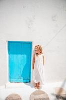 adorable niñita vestida en la calle antigua del típico pueblo tradicional griego con paredes blancas y puertas azules foto