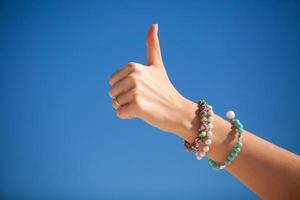 Thumbs up firmar en la mano de una mujer contra el mar turquesa foto