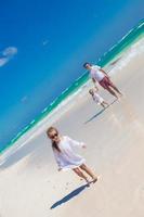 Little girl having fun with her cute sister and young father on white sand beach photo