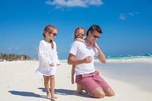 joven padre feliz y pequeñas hijas divirtiéndose en la playa blanca en un día soleado