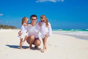 Young happy father and little daughters having fun on white beach in sunny day photo