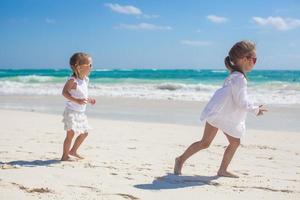 dos hermanitas vestidas de blanco se divierten en la playa de arena tropical foto