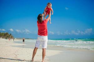 joven padre feliz y su pequeña hija divirtiéndose en la playa blanca en un día soleado