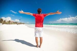 Back view of Young man enjoying the holiday spread his hands on tropical beach photo