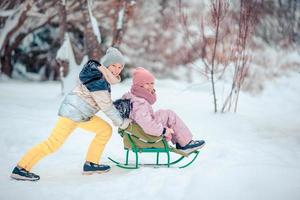 Adorable little happy girls sledding in winter snowy day. photo