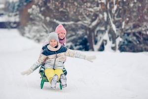 Adorable little happy girls sledding in winter snowy day. photo