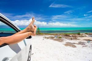 Female barefoot from the window of a car on background tropical beach photo