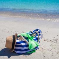 Stripe bag, straw hat, sunblock and frisbee on white sandy tropical beach
