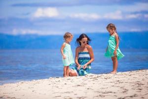 Adorable little girls and young mother relax on tropical white beach in desert island photo