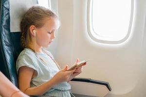 Adorable little girl traveling by an airplane. Cute kid with laptop near window in aircraft photo