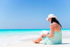 mujer joven leyendo un libro durante la playa blanca tropical foto