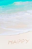 Happy written on sand beach with soft ocean wave on background photo
