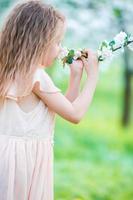 Little beautiful girl enjoying smell of blooming apple tree in a flowering spring garden photo